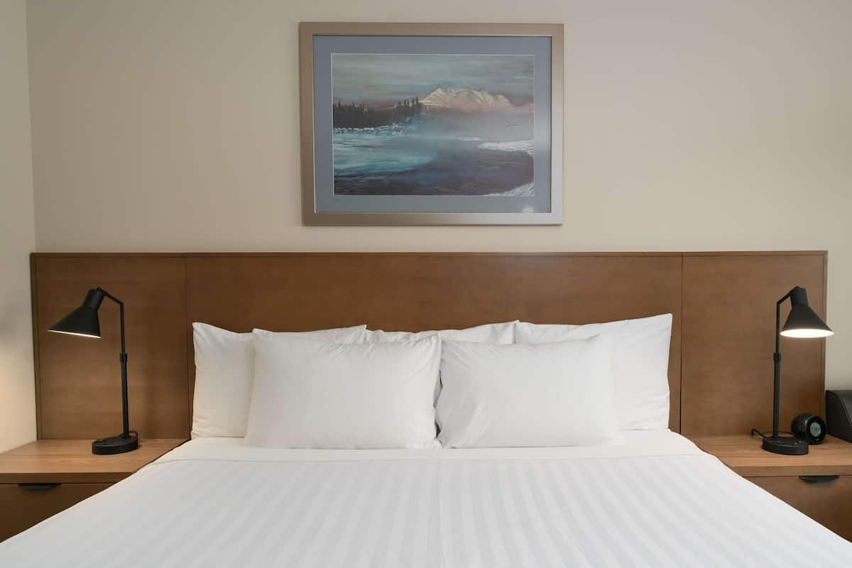 A hotel room with a large bed, two bedside lamps, and a framed landscape painting on the wall.
