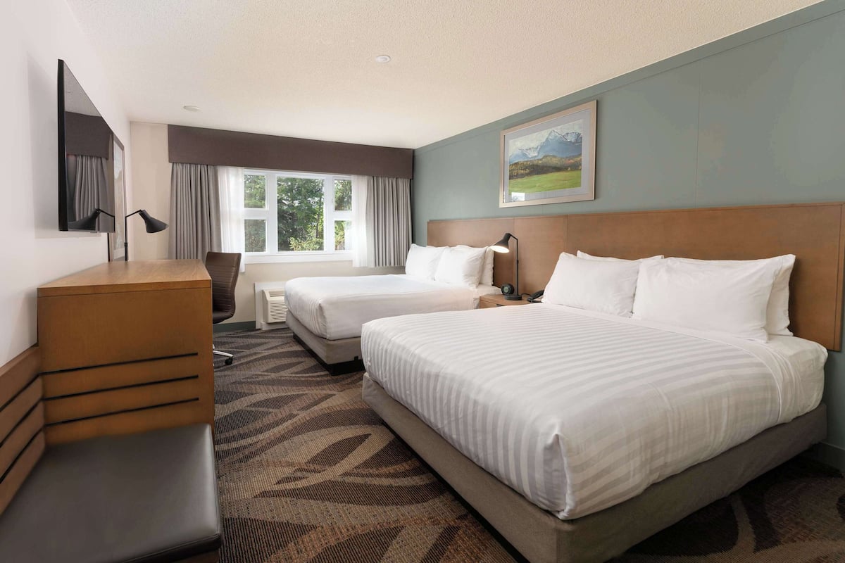 A hotel room with two beds, a desk, a chair, a dresser, and a painting on the wall.