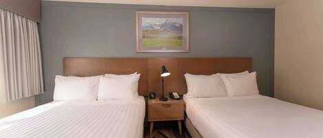 A hotel room with two beds, a nightstand with a lamp, a phone, and a framed picture on the wall.