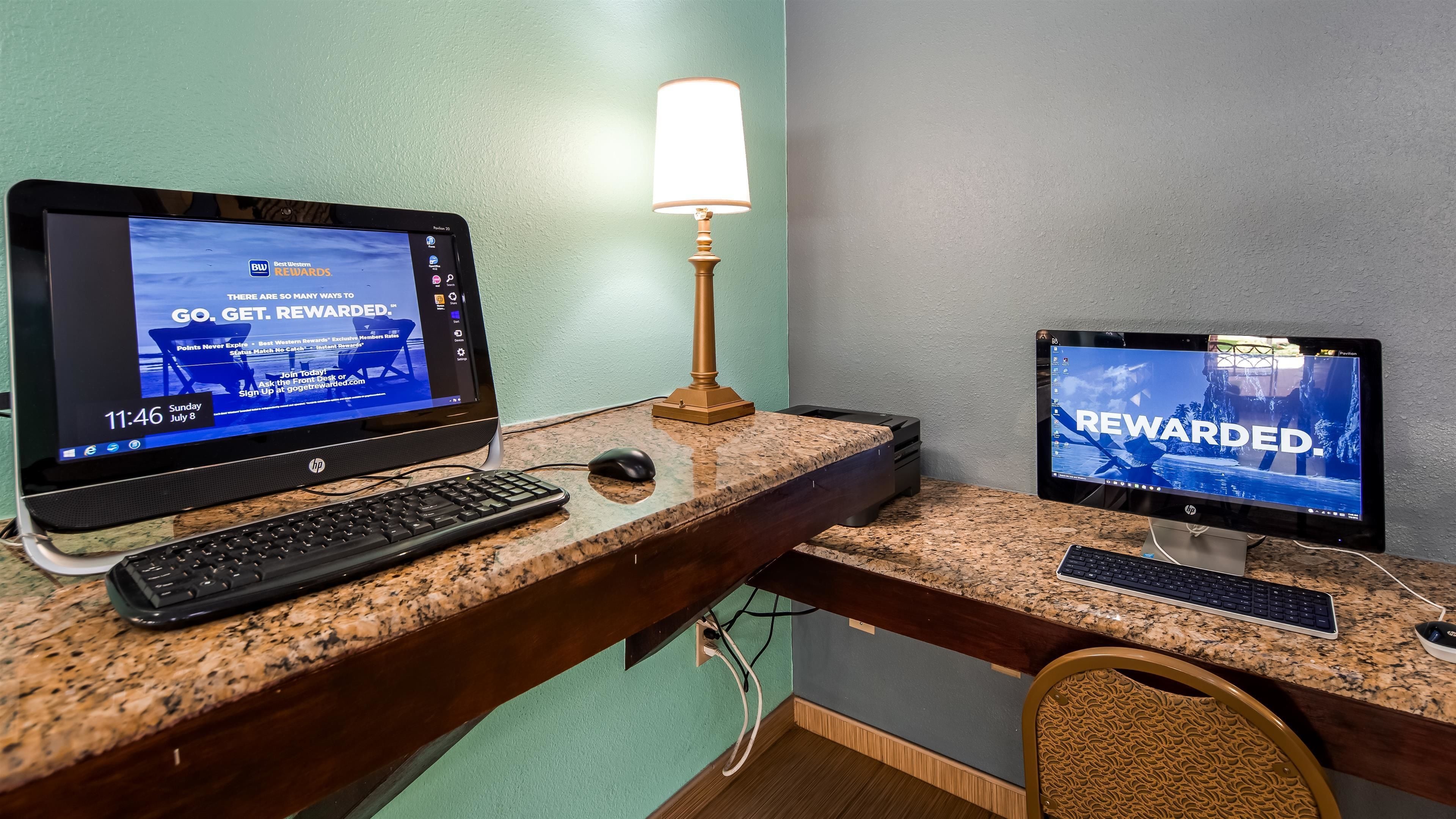 A hotel room with a desktop computer setup, including two monitors, a keyboard, and a mouse on a granite countertop.