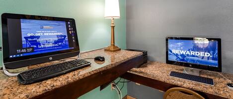 A hotel room with a desktop computer setup, including two monitors, a keyboard, and a mouse on a granite countertop.