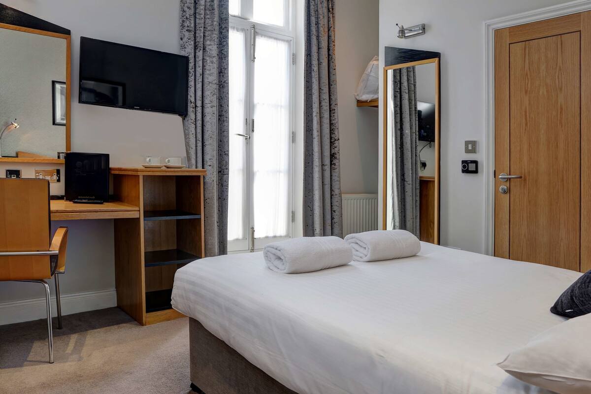 A hotel room with a bed, a desk with a computer, a TV, and a wardrobe.