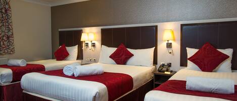 A hotel room with three beds, each with white linens and red accents, equipped with bedside lamps and a telephone.