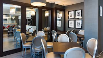 A modern dining area with multiple tables and chairs, framed pictures on the wall, and a large mirror reflecting the space.