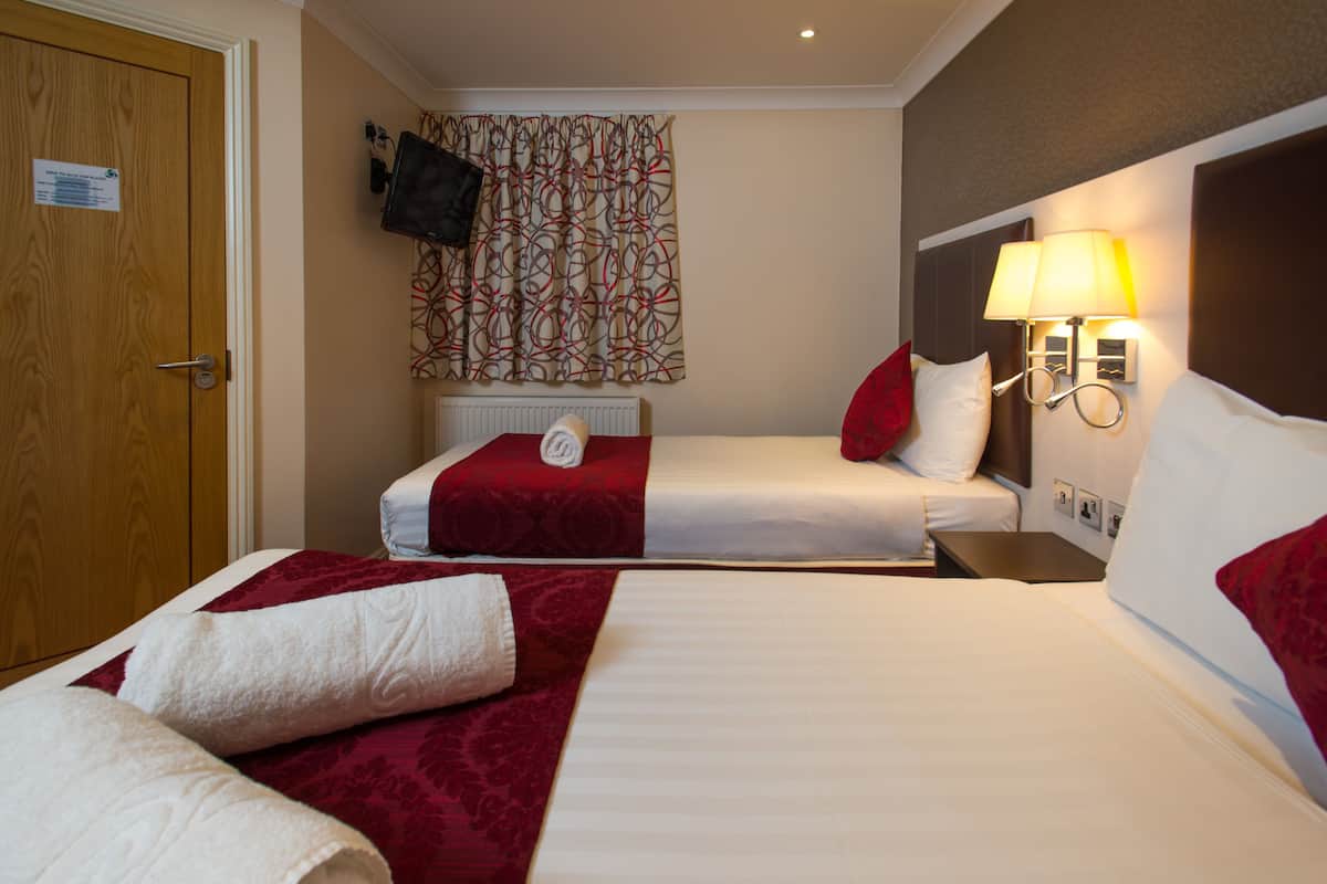 A hotel room with two beds, a television mounted on the wall, and a lamp on the nightstand.