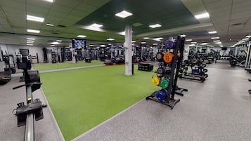 Ein Fitnessstudio mit grünem Kunstrasen, Gewichthebergeräten und verschiedenen Trainingsmaschinen.