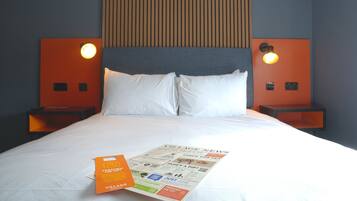 Una habitación de hotel con una cama, dos mesitas de noche, un cabecero y una lámpara fijada a la pared.
