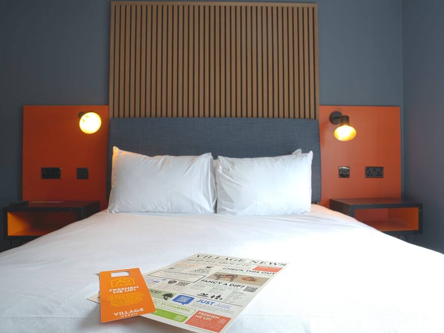 A hotel room with a bed, two nightstands, a headboard, and a wall-mounted light fixture.