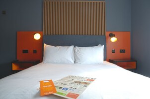 Una habitación de hotel con una cama, dos mesitas de noche, un cabecero y una lámpara fijada a la pared.