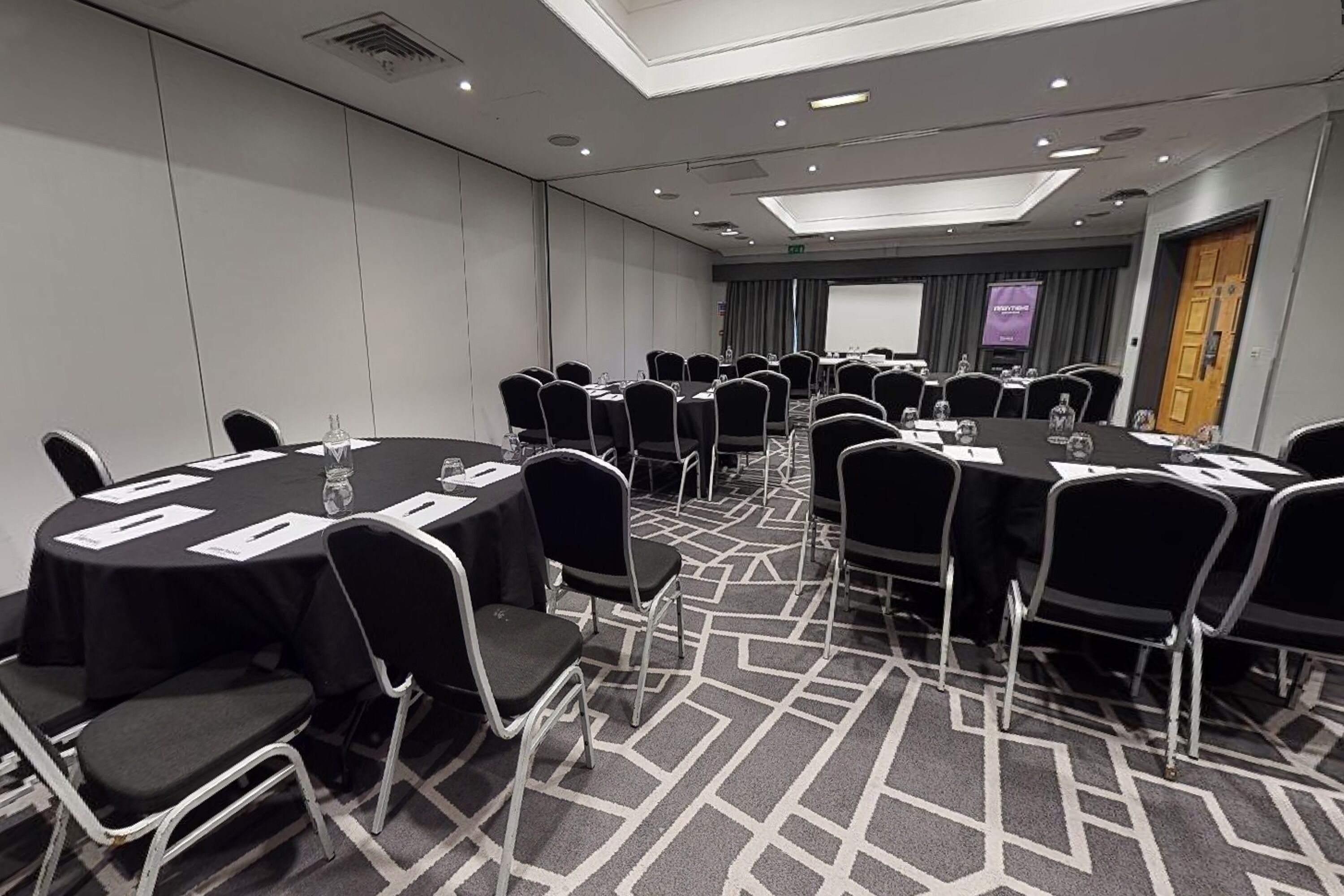 A conference room with round tables, black chairs, and a carpeted floor.