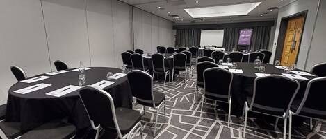 Una sala de conferencias con mesas redondas, sillas negras y suelo alfombrado.