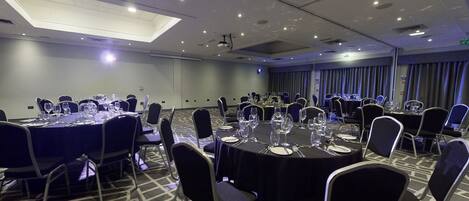 Une salle de conférence avec des tables rondes, des chaises et un luminaire au plafond.