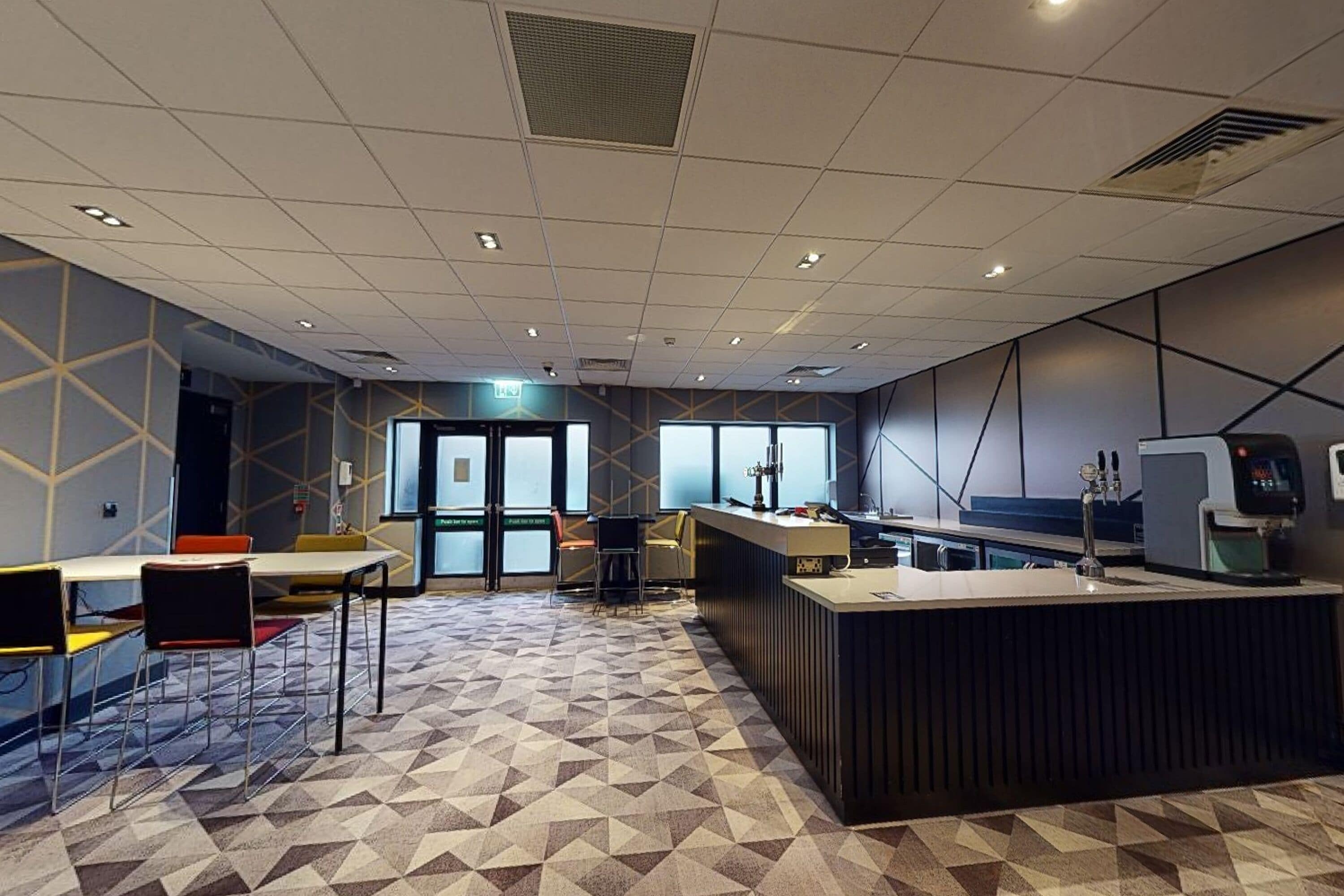 A modern office space with a geometric patterned floor, a reception area with a counter and computer, and a seating area with chairs and tables.