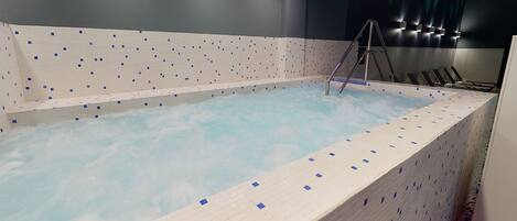 A large indoor swimming pool with a tiled edge, a ladder, and a wall with a patterned design.