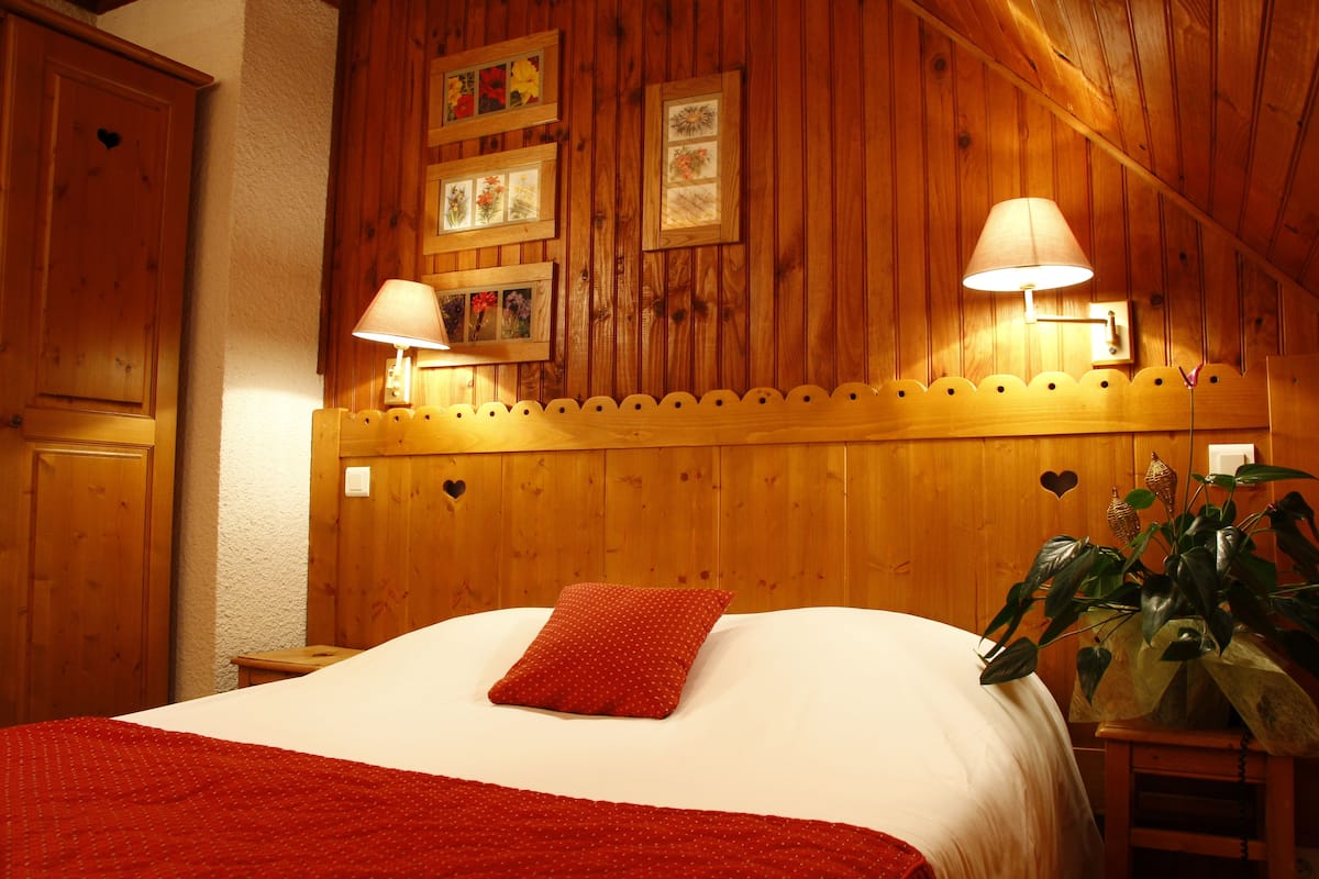 A wooden-themed bedroom with a bed, two wall-mounted lamps, and framed pictures.