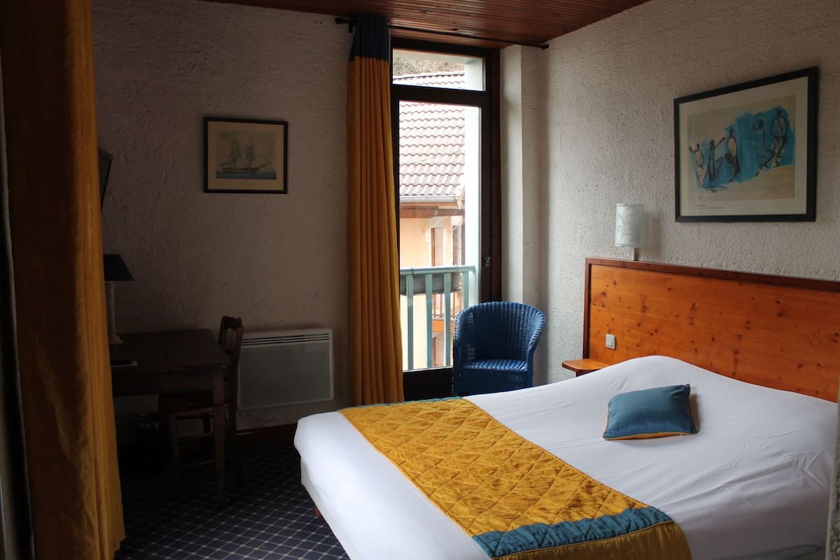 A hotel room with a bed, a chair, a desk, and a window with curtains.