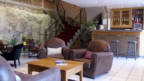 A lobby with leather armchairs, a wooden coffee table, a staircase, and a bar area with bottles. - Hotel des Marquisats Annecy (Annecy)