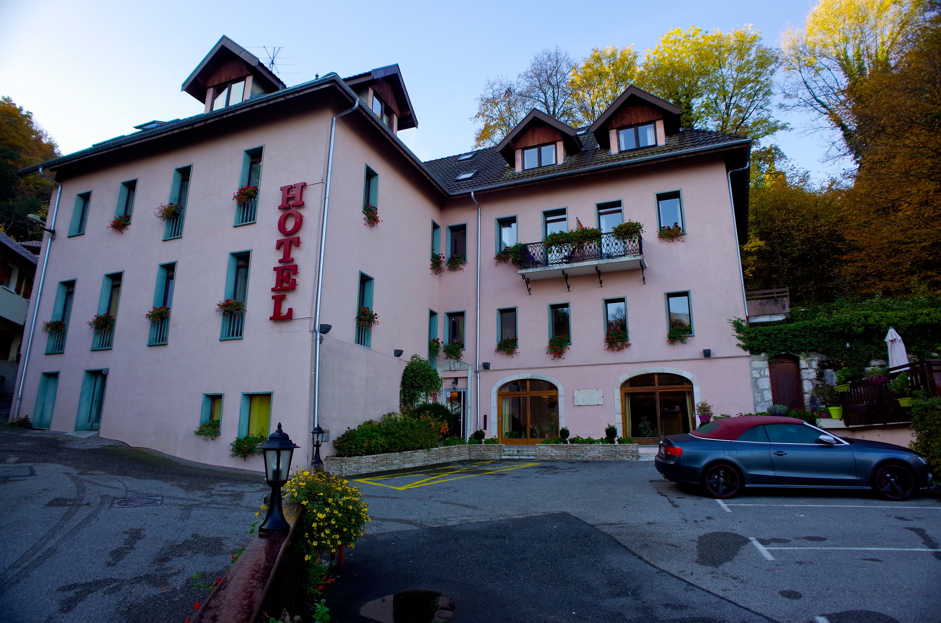Un hotel rosa con techo rojo, múltiples ventanas y un coche estacionado adelante.