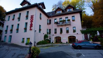 Un hotel rosa con techo rojo, múltiples ventanas y un coche estacionado adelante.