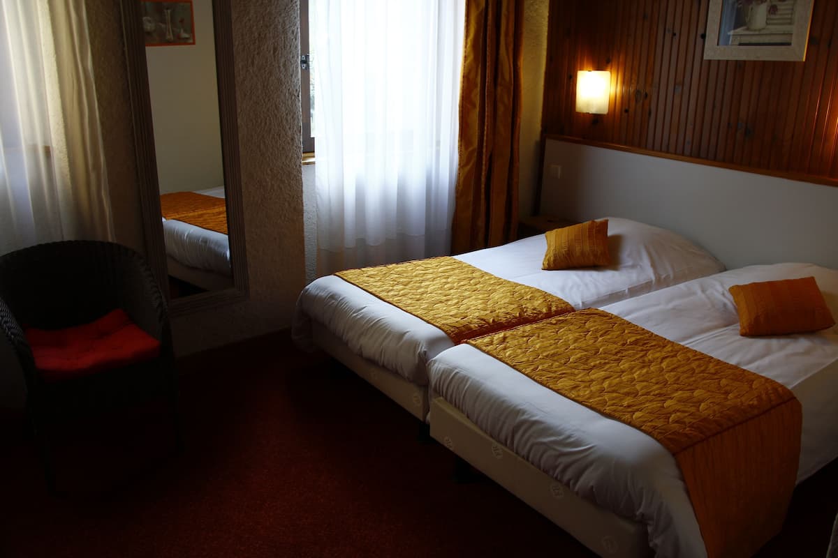 A hotel room with two beds, a chair, and a mirror.