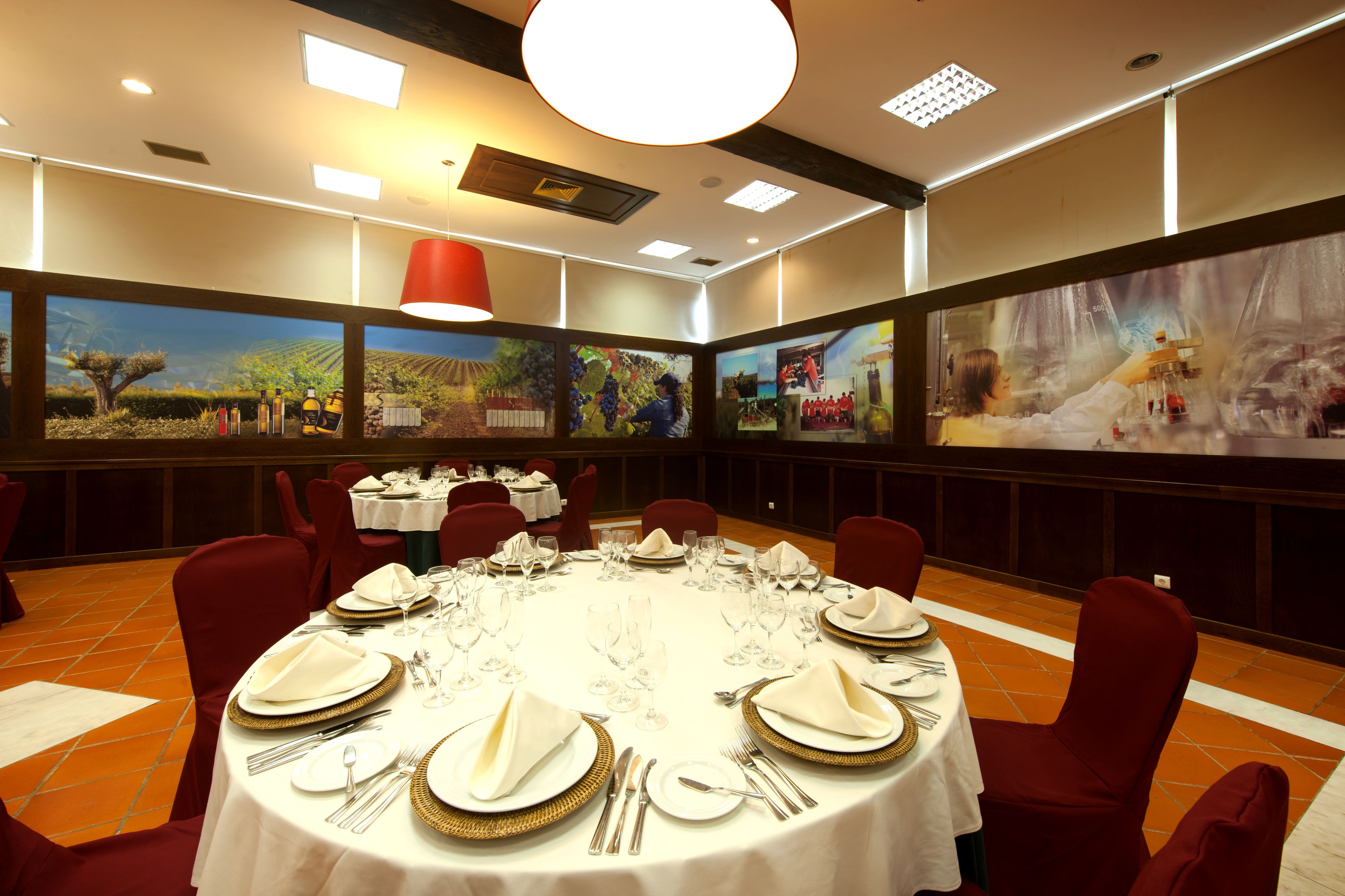 Un salón de conferencias con mesas redondas dispuestas para un evento formal, con manteles blancos, platos con borde dorado y sillas rojas.