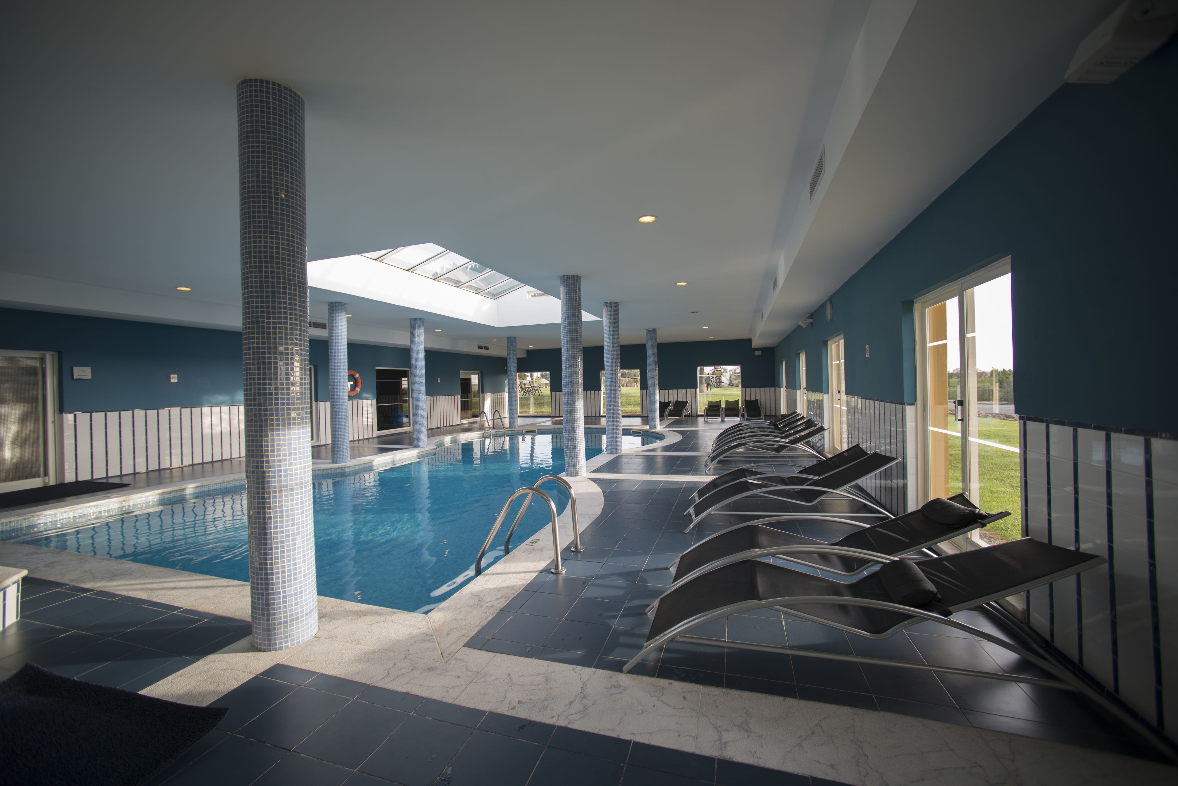 Una piscina con tragaluces, paredes enlosadas y tumbonas.