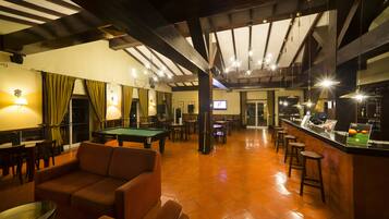 Sala de billar con mesa de pool, sofás y una zona de bar con taburetes.