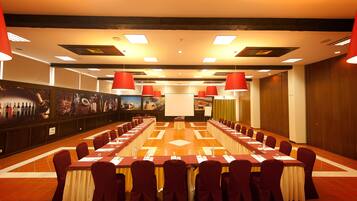 A conference room with a long table, red chairs, and a projector screen.