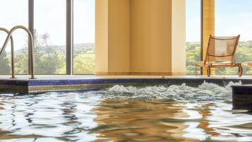 A hot tub with a view of a forested landscape through large windows.