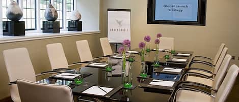 Un salón de conferencias con una mesa de vidrio, sillas blancas y una pantalla que muestra