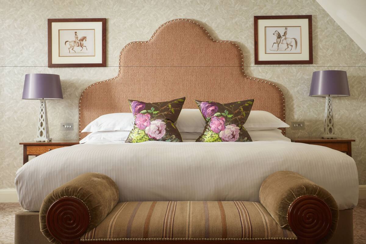 A neatly made bed with floral pillows, a wooden headboard, and a bench at the foot of the bed.