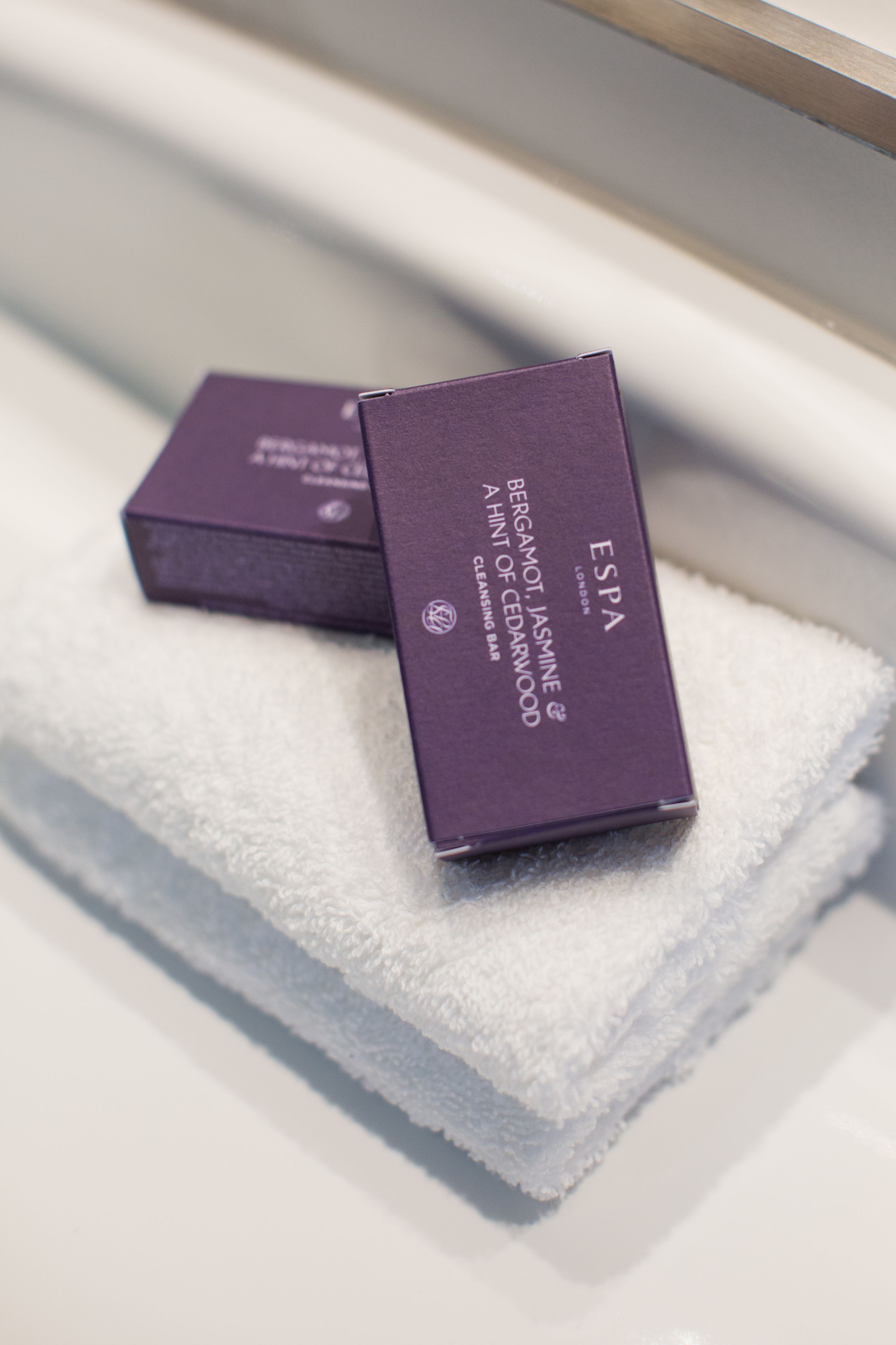 Deux boîtes violettes portant l’inscription « BERGAMOTE, JASMIN ET UNE NOTE LÉGÈRE DE BOIS DE CÈDRE » sont posées sur une serviette blanche.