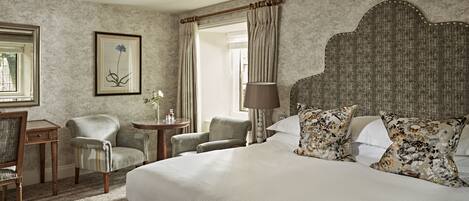 A hotel room with a large bed, two armchairs, a small table, a lamp, and a framed picture on the wall.