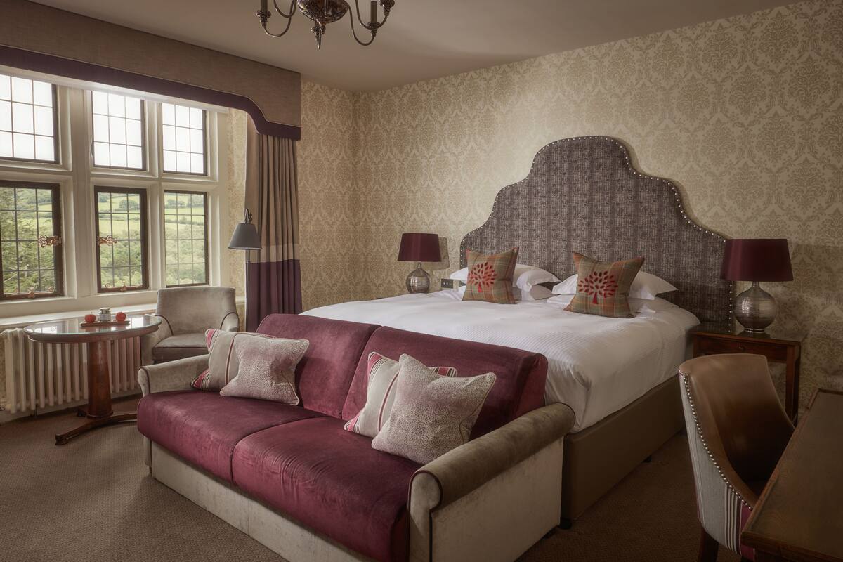A hotel room with a large bed, a sitting area with a sofa, a small table, and a chair.