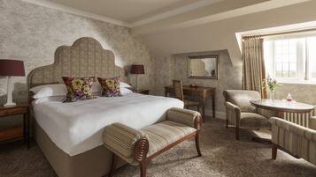 A hotel room with a large bed, a wooden chair, a small table, a desk, and a window with curtains.