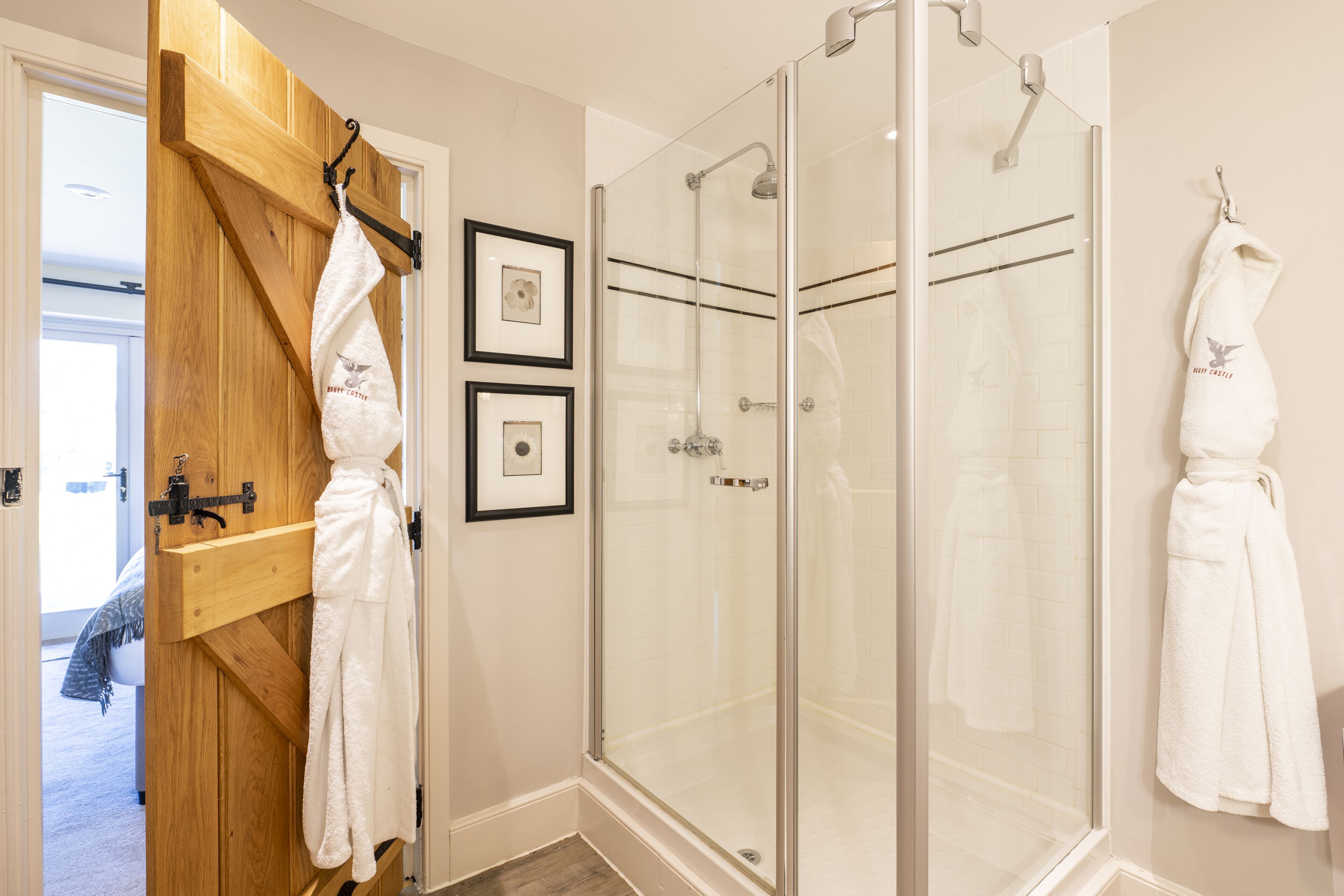 A modern bathroom with a glass shower enclosure, wooden door, and two framed pictures on the wall.