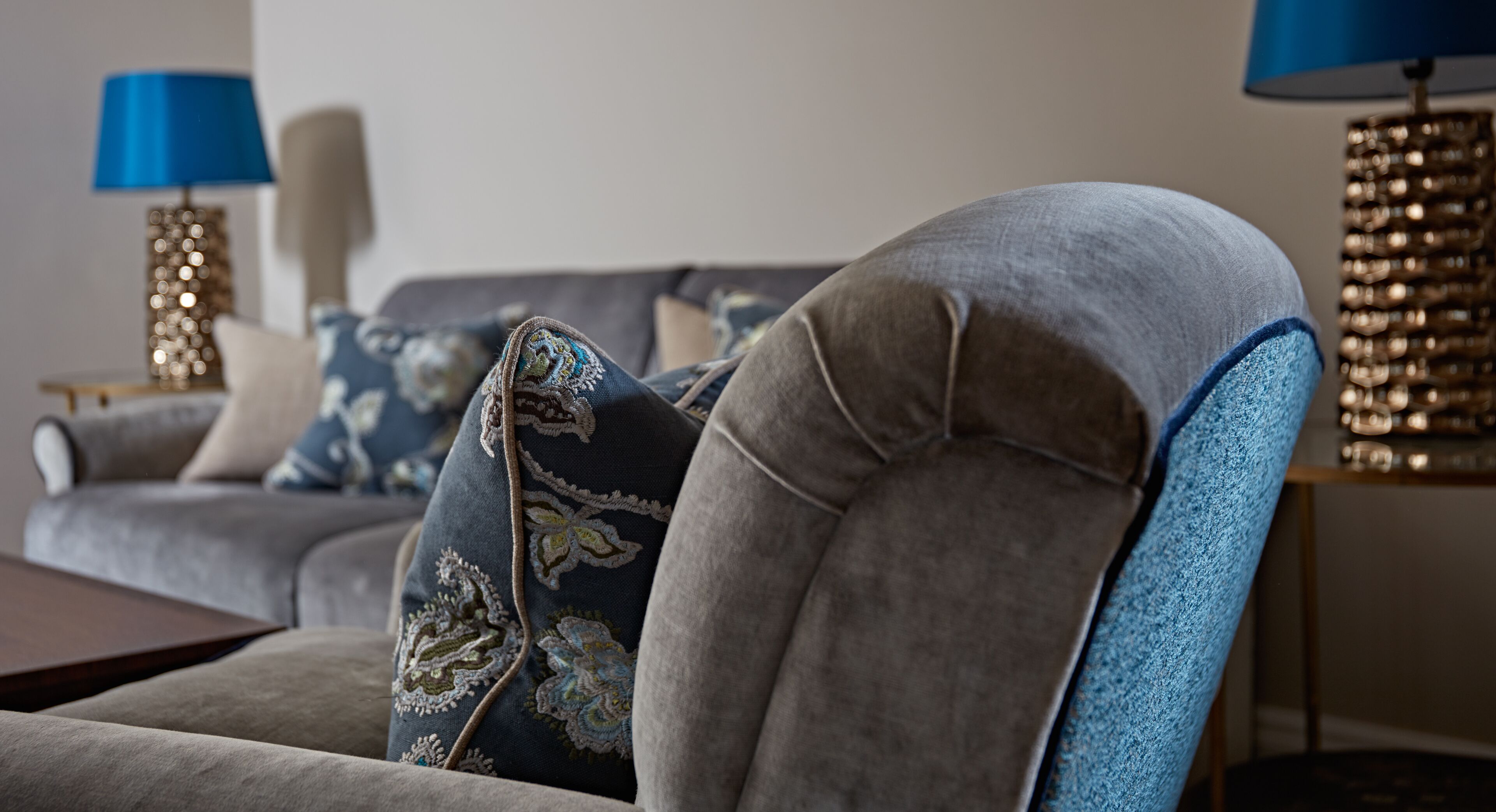 A living room with a grey sofa, a blue armchair, and decorative lamps.