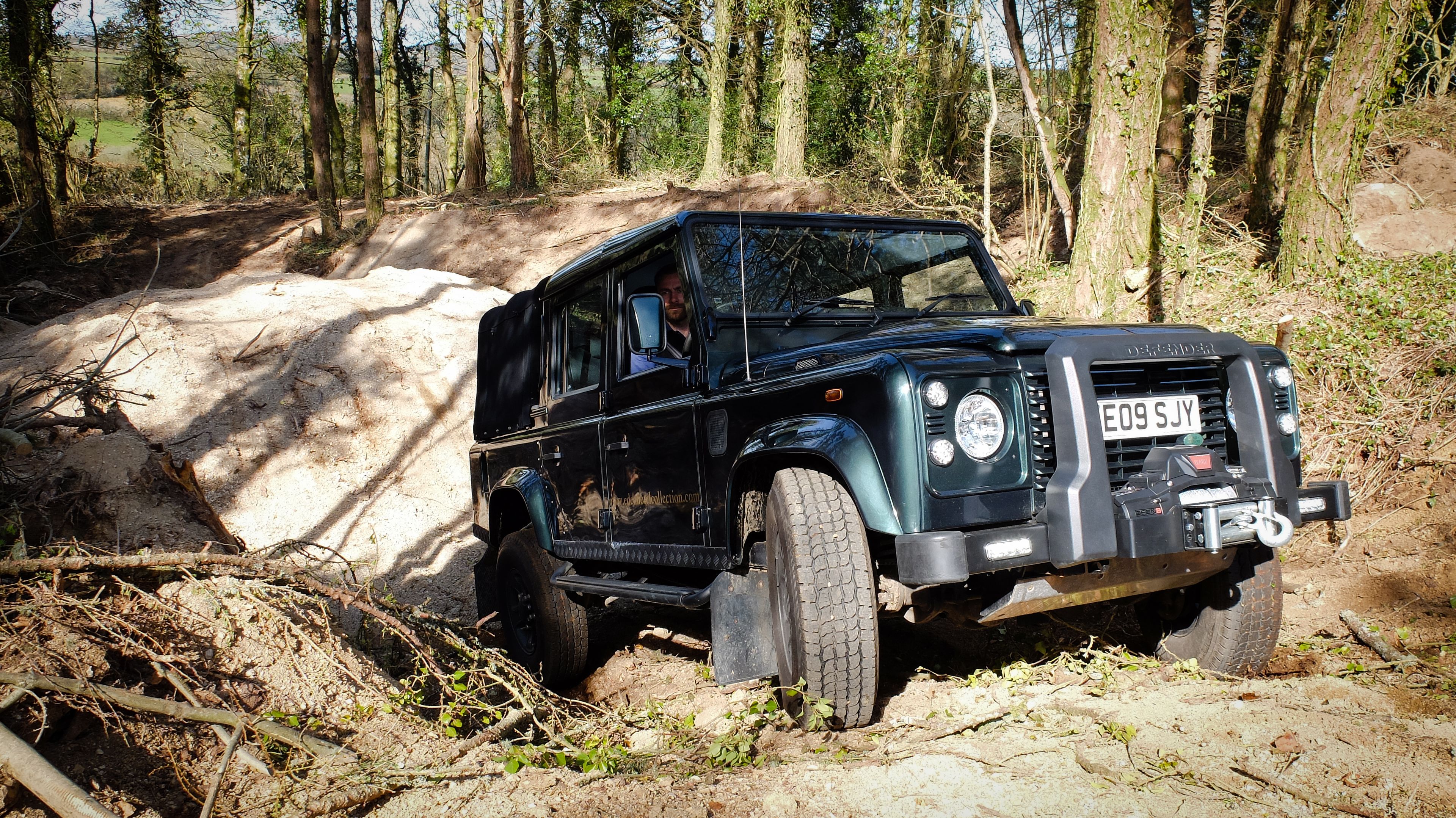 A black off-road vehicle with a license plate E09 SJY, parked on a dirt path surrounded by trees.