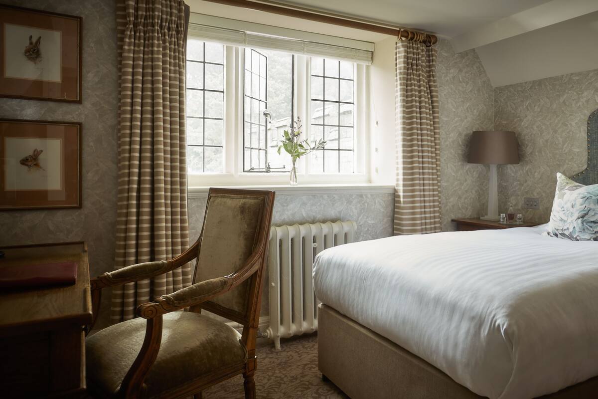 A bedroom with a large bed, a chair, a lamp, and a window with curtains.