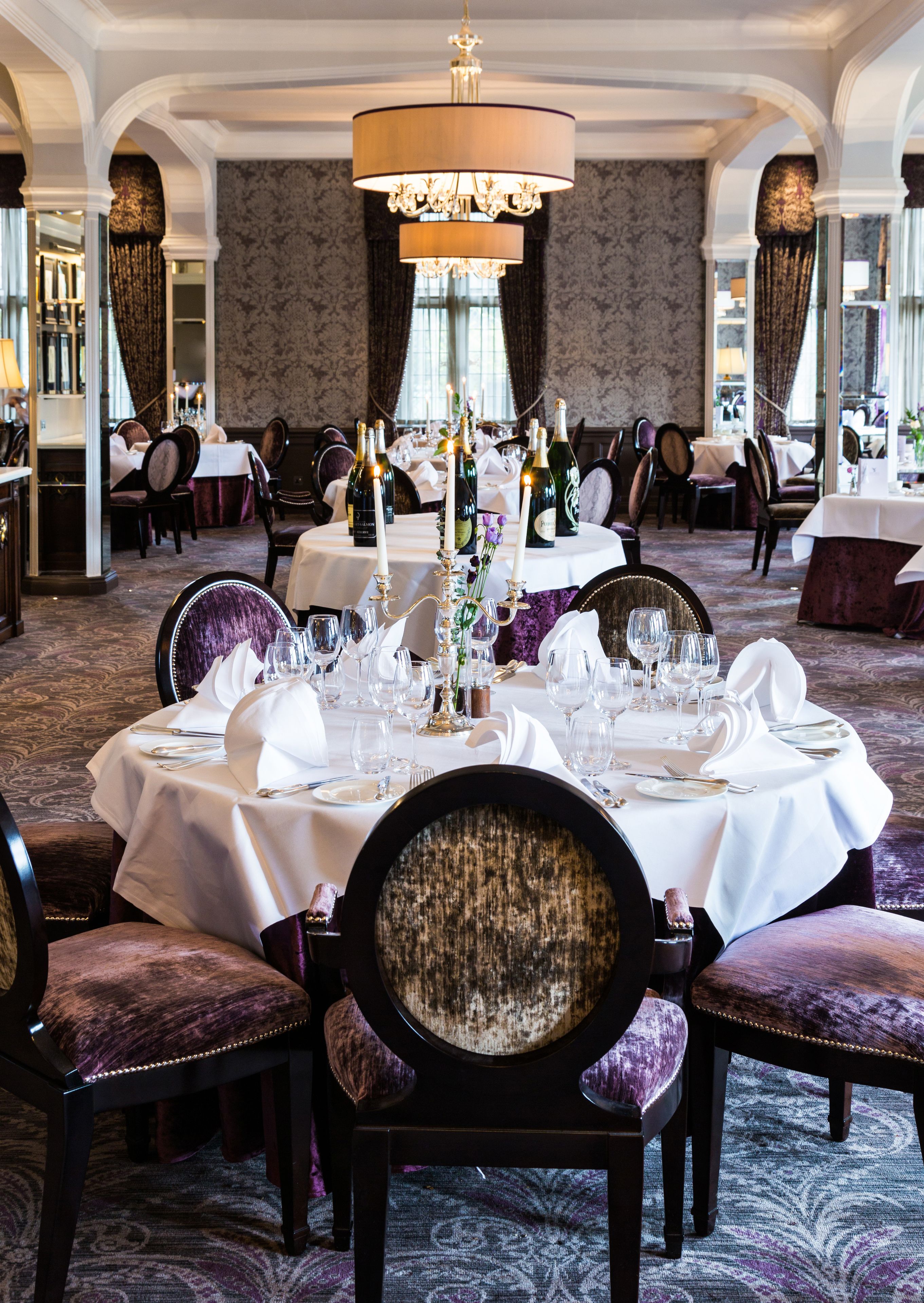 A formal dining room with round tables, white tablecloths, and purple upholstered chairs.