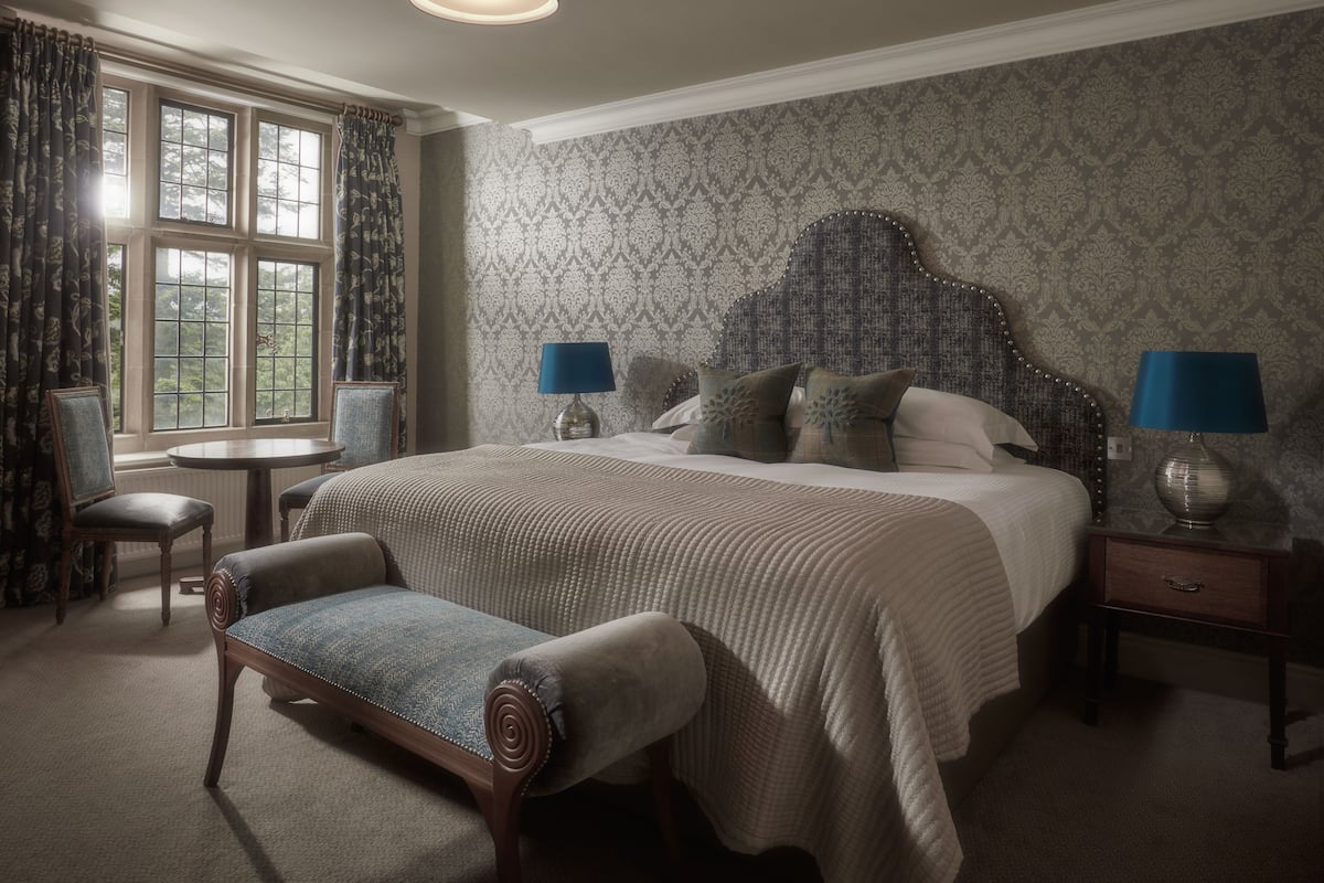 A bedroom with a large bed, two bedside tables with lamps, a chair, and a window with curtains.