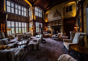 A spacious lounge with high ceilings, large windows, and a fireplace. - Bovey Castle (Newton Abbot)