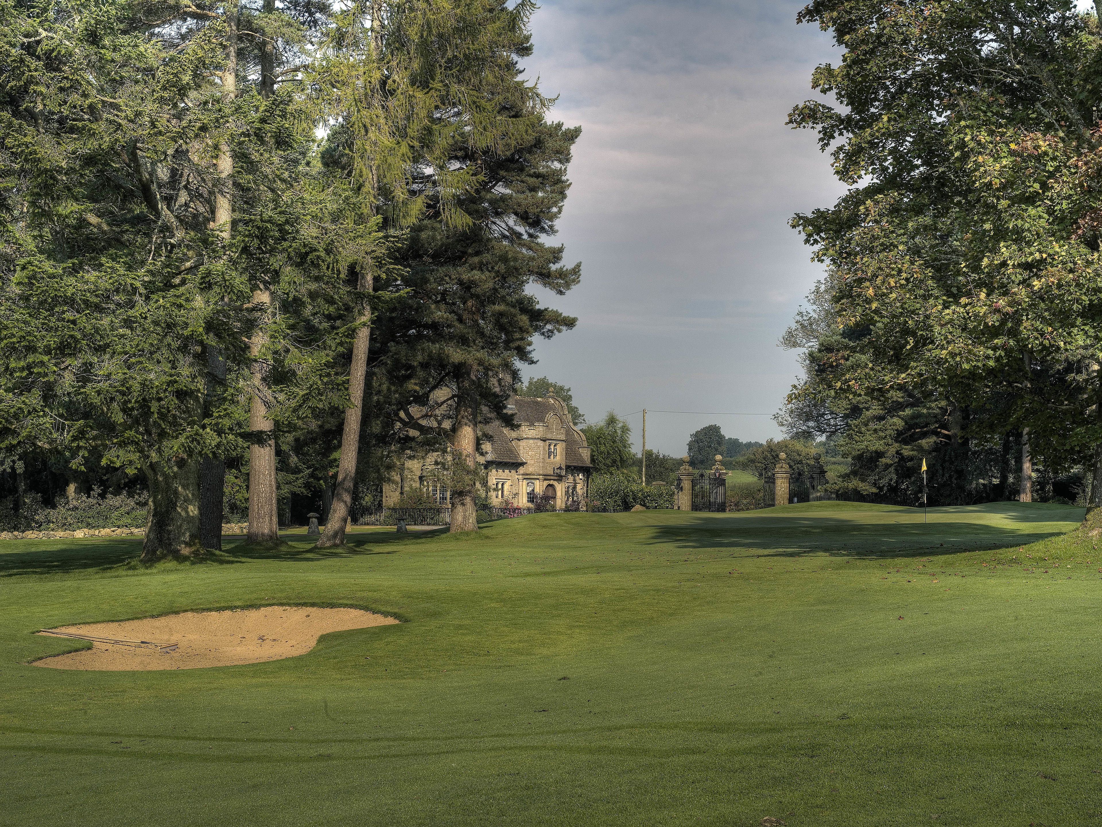 A golf course with a clubhouse, surrounded by tall trees and a well-maintained lawn.