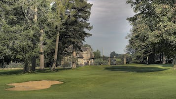 A golf course with a clubhouse, surrounded by tall trees and a well-maintained lawn.
