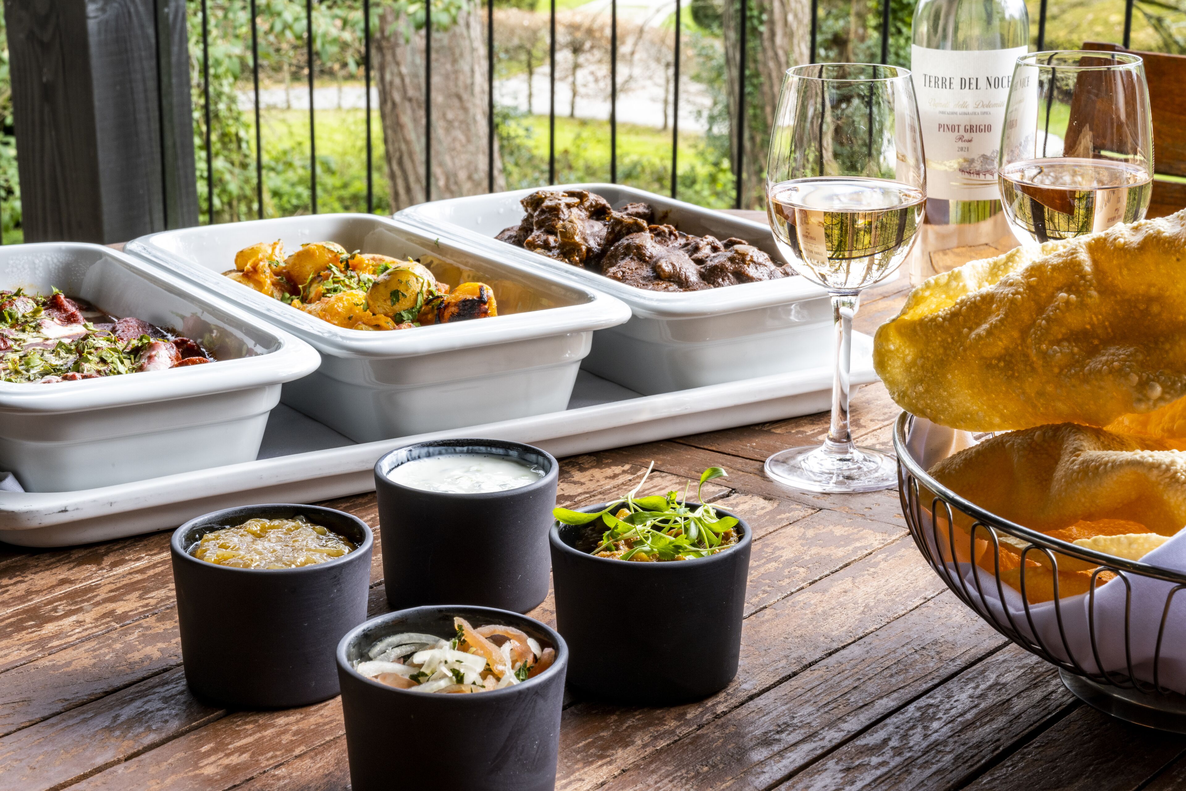 A wooden table with various dishes, glasses of wine, and a bowl of bread.