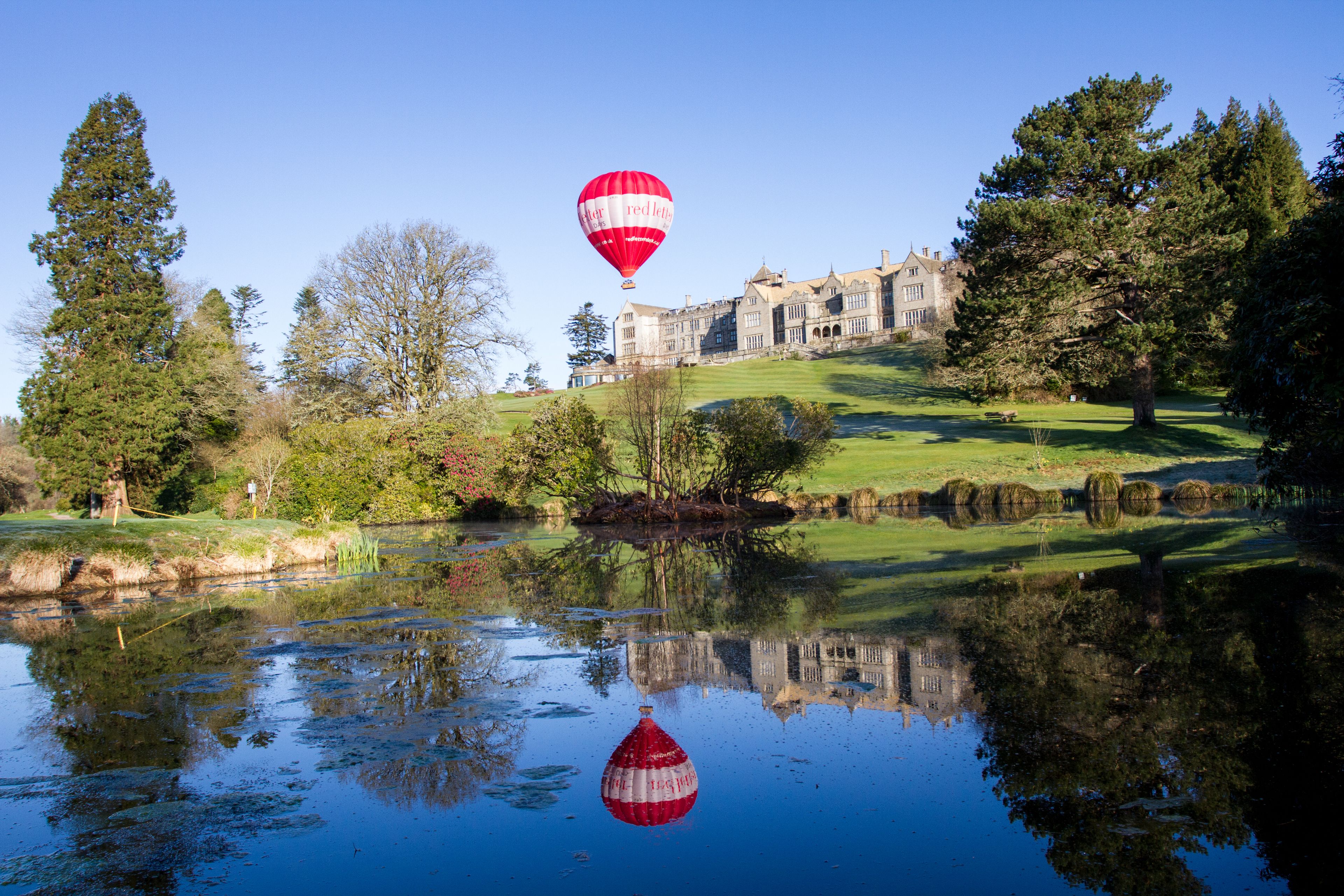 Un globo aerostático sobre un cuerpo de agua, con un edificio grande al fondo.
