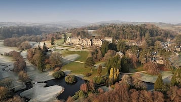 A large estate with a prominent manor house surrounded by landscaped gardens, a river, and rolling hills in the background.