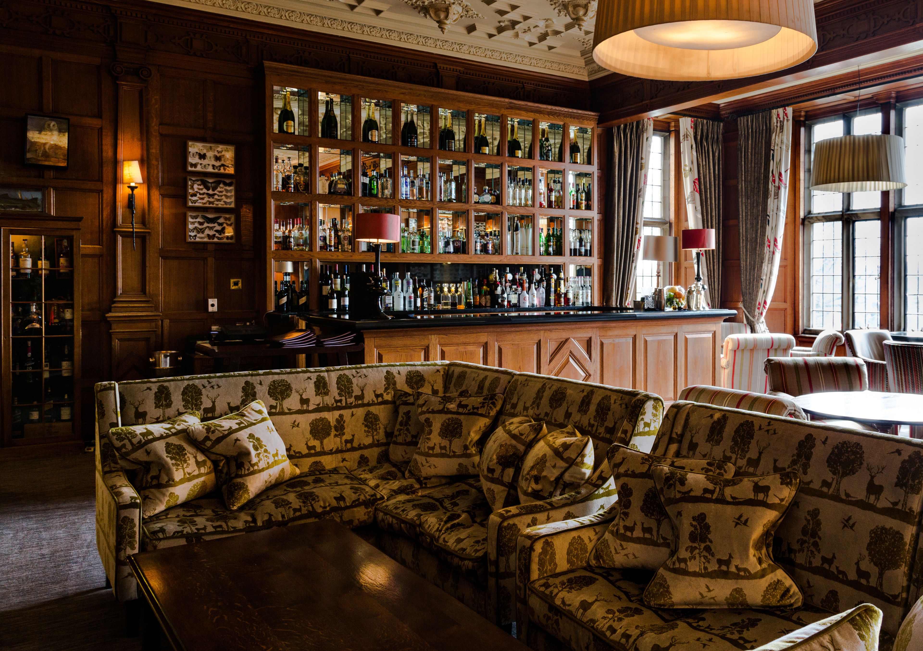 A bar area with a wooden bar counter, shelves of bottles, and a patterned sofa in the foreground.
