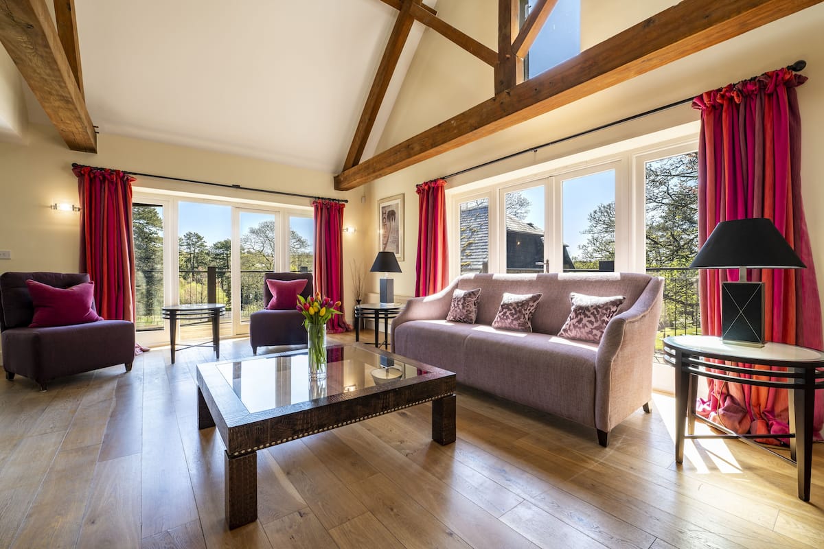 A spacious living room with a wooden floor, a sofa, a coffee table, and a balcony with red curtains.