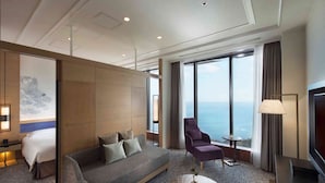 Une chambre d’hôtel moderne, dotée d’un grand lit, d’un canapé, d’un fauteuil, d’une petite table et offrant une vue sur la mer.